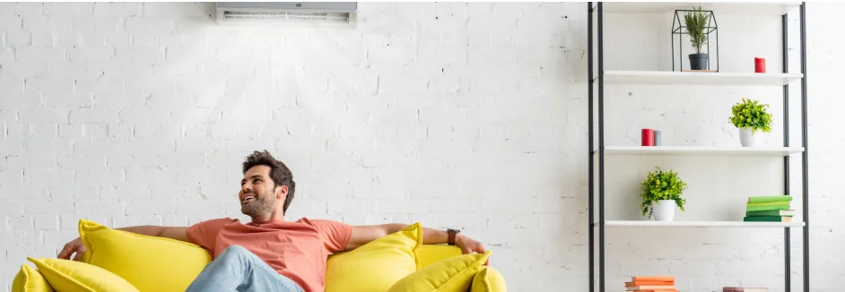Person entspannt auf gelbem Sofa unter einer Klimaanlage.